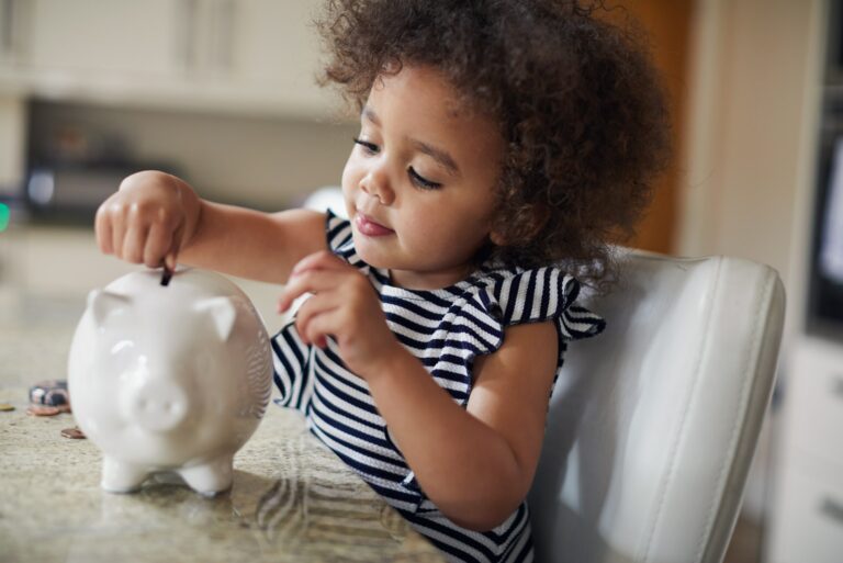 Child Putting Coins Into Piggy Bank